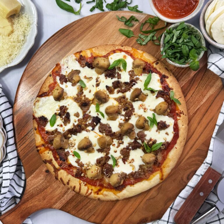 A Garlic Mushroom Pizza on a round wooden cutting board on a counter top.