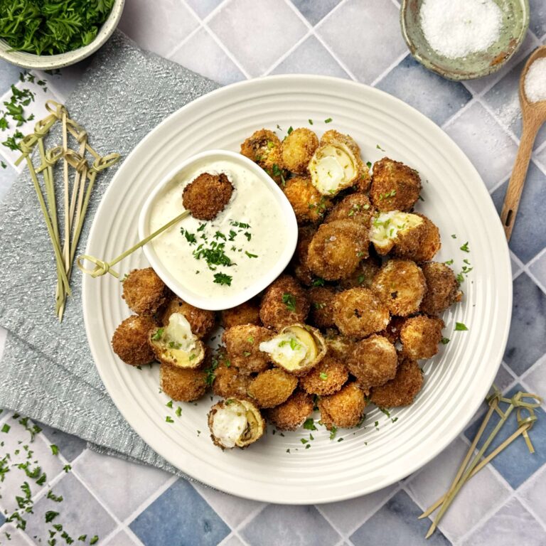A white plate with Cheesy Mushroom Poppers and a side of dipping sauce,