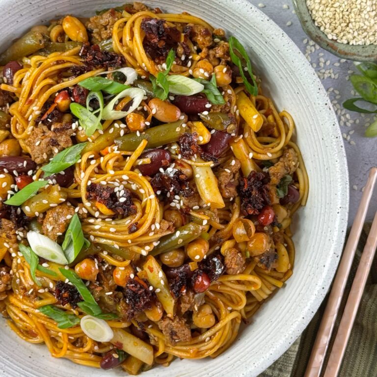A white bowl with Chili Crunch Noodles with ground pork and Five Bean Salad