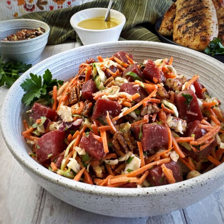 A big white bowl of Sweet Beet and Carrot Slaw, with a sid of Honey Mustard Vinaigrette Dressing.