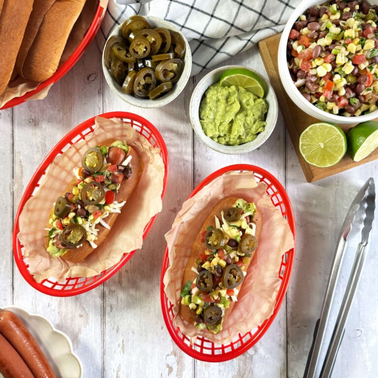 Loaded Tex Mex Hot Dogs with Pickled Jalapenos in two red plastic baskets on a table.