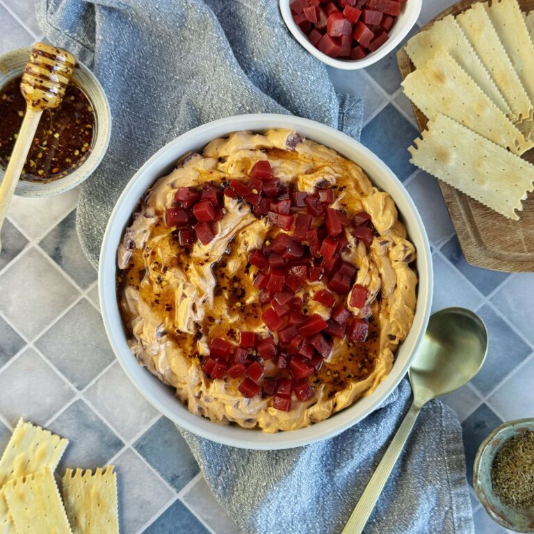 A white bowl with Whipped Cream Cheese Dip with Sweet Beets and Hot Honey with a board of crackers.