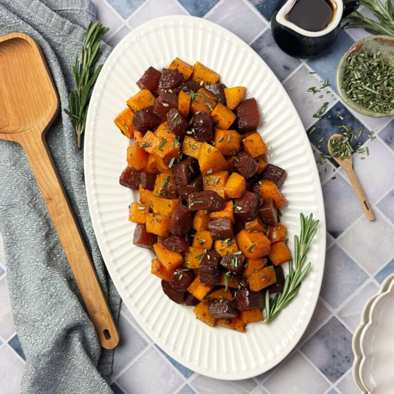 Maple Roasted Butternut Squash and Sweet Beets on a white oval plate with a wooden serving spoon to the left.