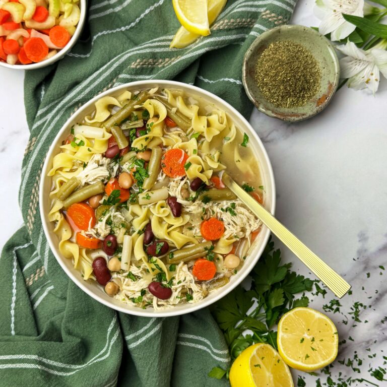 A white dinner bowl filled with the Slow Cooker Chicken noodle soup with Five Bean Salad.