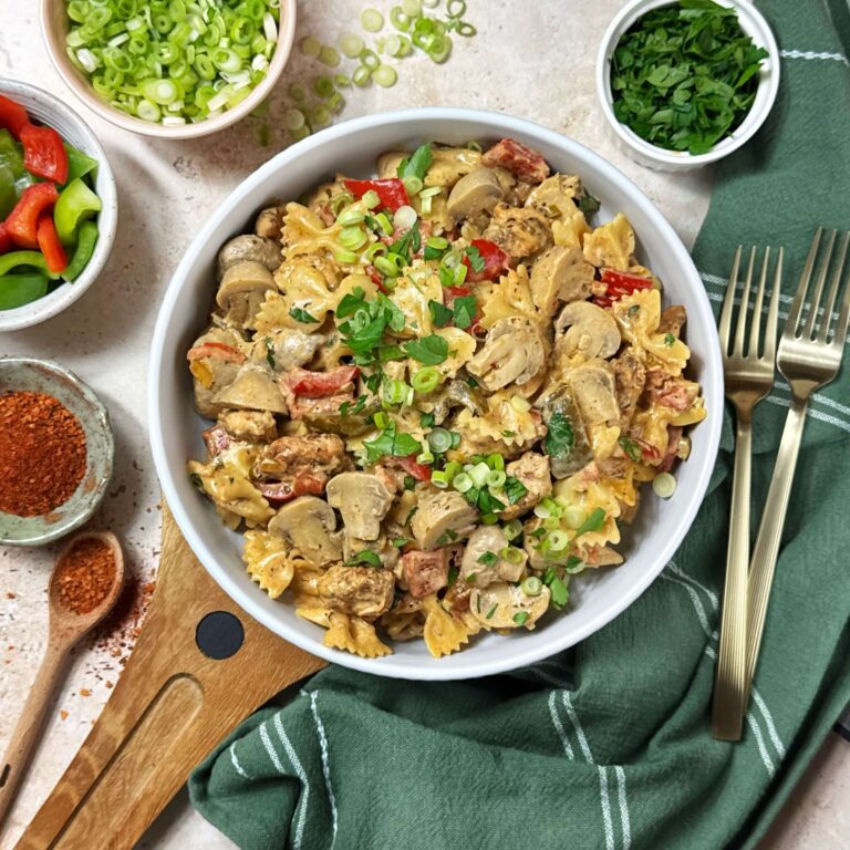Bowl of Creamy Cajun Chicken and Marinated Mushroom Pasta in a white dinner bowl with a wooden cutting board underneath it.