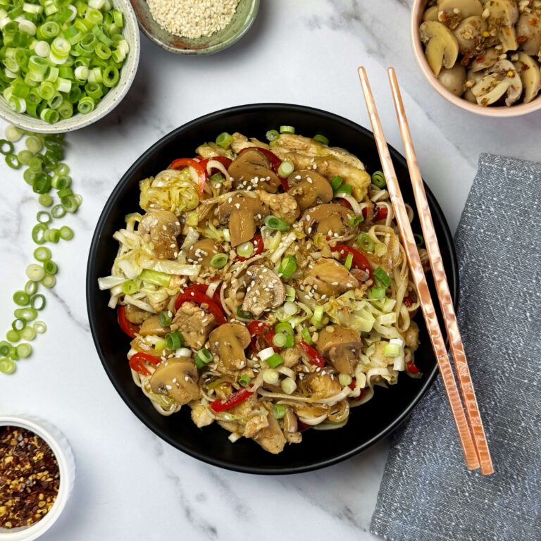 A black dinner bowl filled with Stir-fried Noodles with Chicken, Cabbage and Marinated Mushrooms |With Chop sticks.