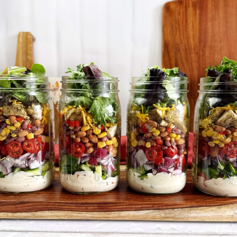 Four mason jars filled with Meal Prep Salad with Chicken and Cowboy Caviar on a wooded tray.