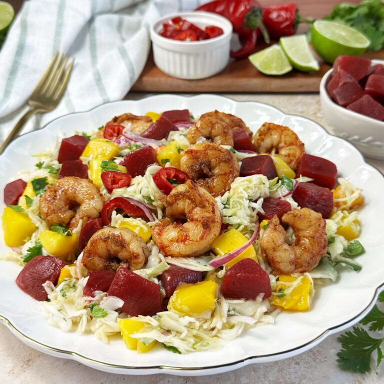 Mango, sweet beet, and cabbage salad topped with grilled shrimp and honey lime vinaigrette, served as a fresh and colorful summer meal.
